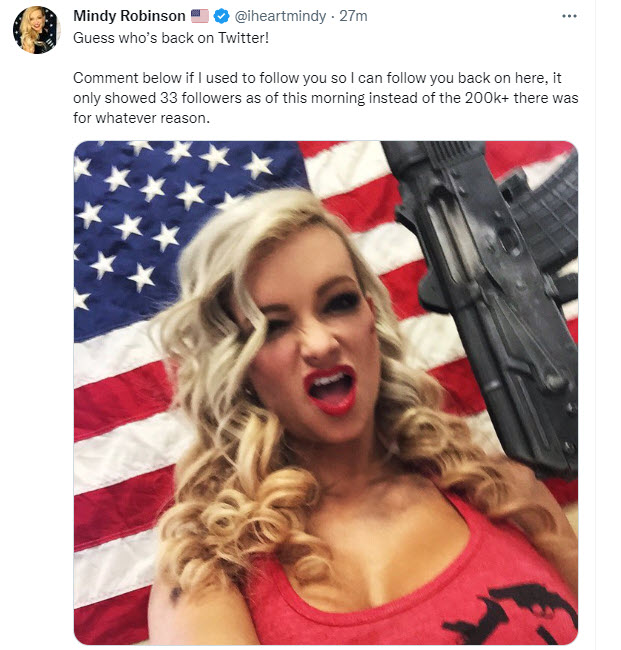 Mindy Robinson in front of an American flag holding a gun and winking