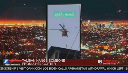 A screenshot from a video with a helicopter in midair from the OAN show In Focus with Stephanie Hamill. The chyron reads "Taliban hangs someone from a helicopter" 
