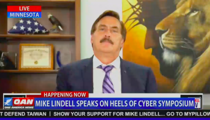 An OAN screenshot of MyPillow CEO Mike Lindell on "Lindell TV", with a folded U.S. flag behind his right shoulder, and an airbrushed portrait of Jesus Christ and a lion behind his left shoulder. Chyron reads "Mike Lindell speaks on heels of cyber symposium"